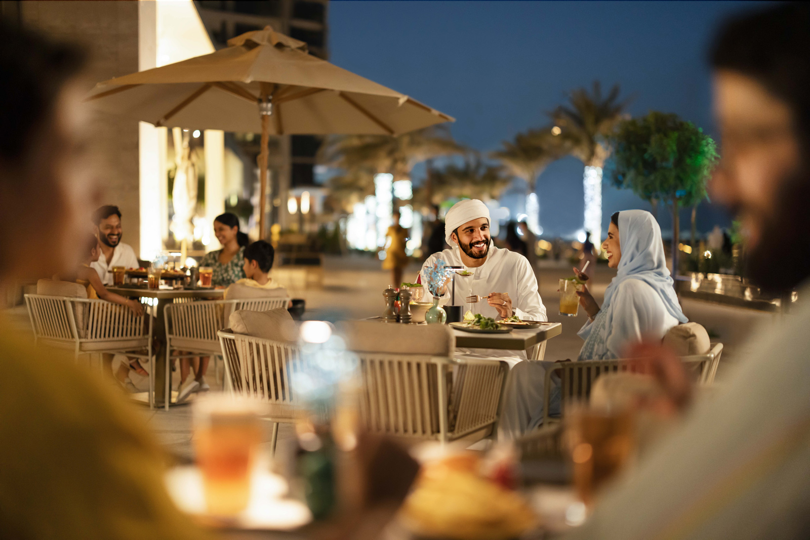 People sitting at tables with umbrellas and trees in the background, Saadiyat Island dining and leisure