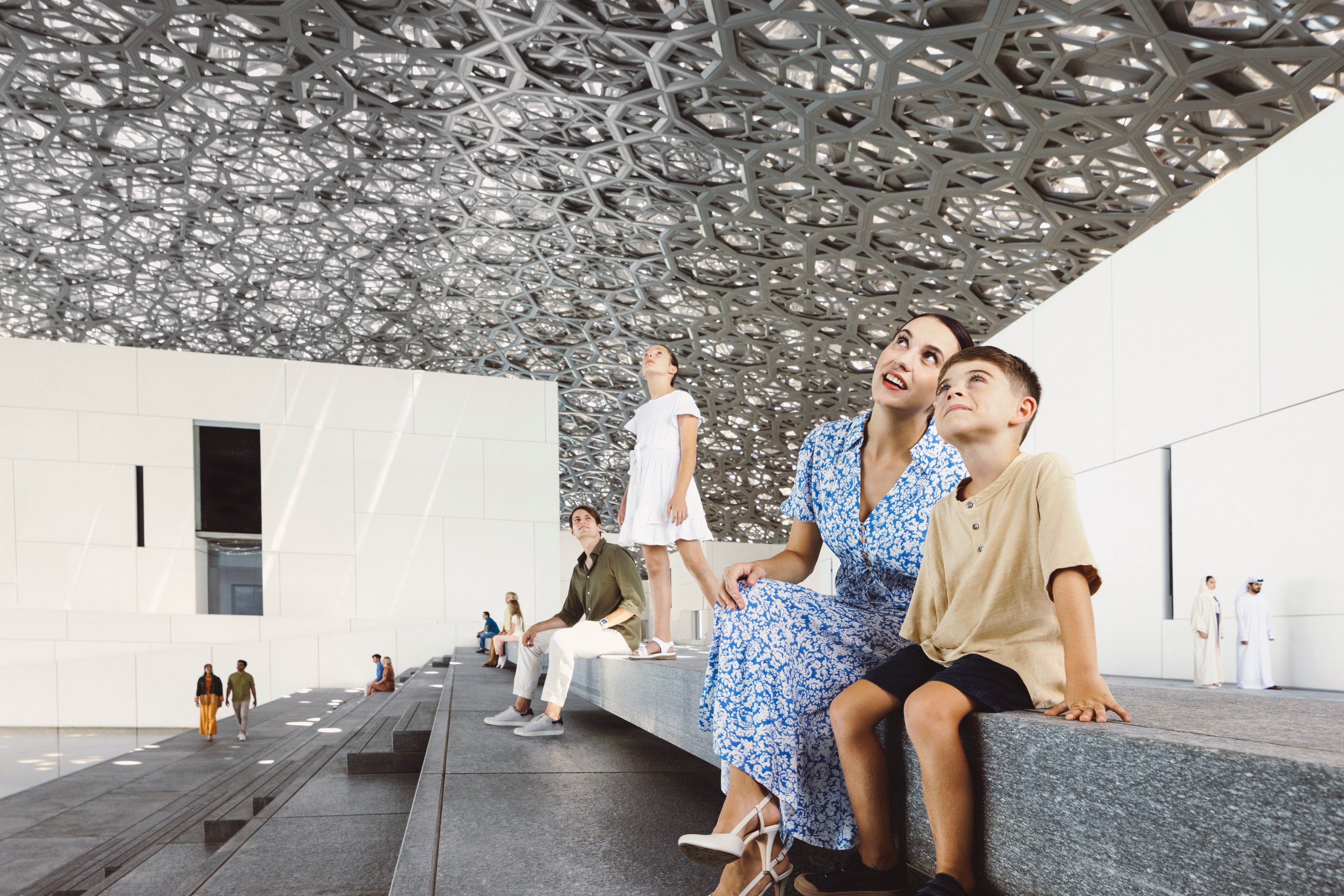 عائلة أجنبية من أربعة أفراد تتأمل الأعجوبة المعمارية أعلى الدرج الخارجي لمتحف اللوفر أبوظبي