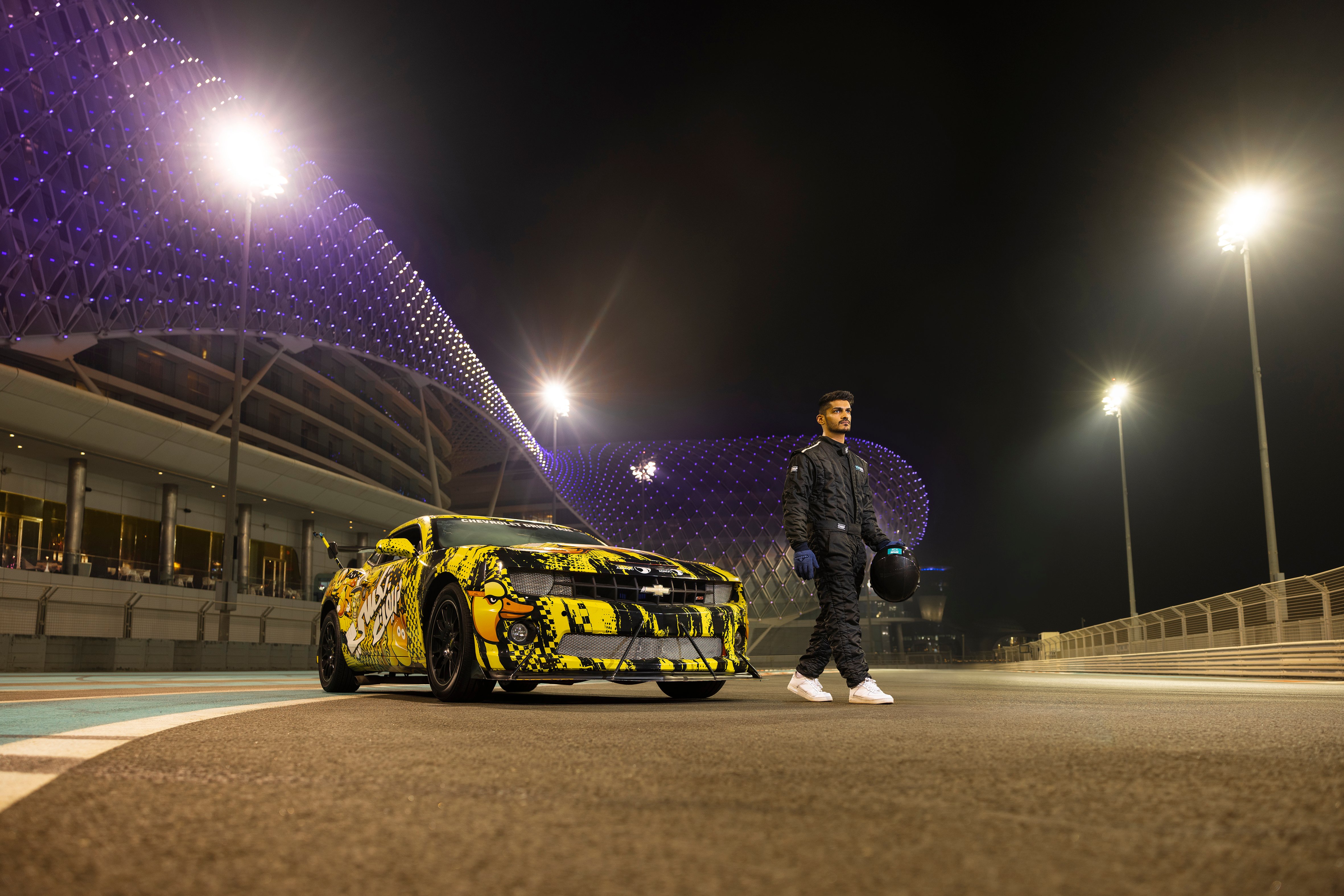 A racecar driver standing next to a custom-painted car at Yas Marina Circuit, Abu Dhabi.