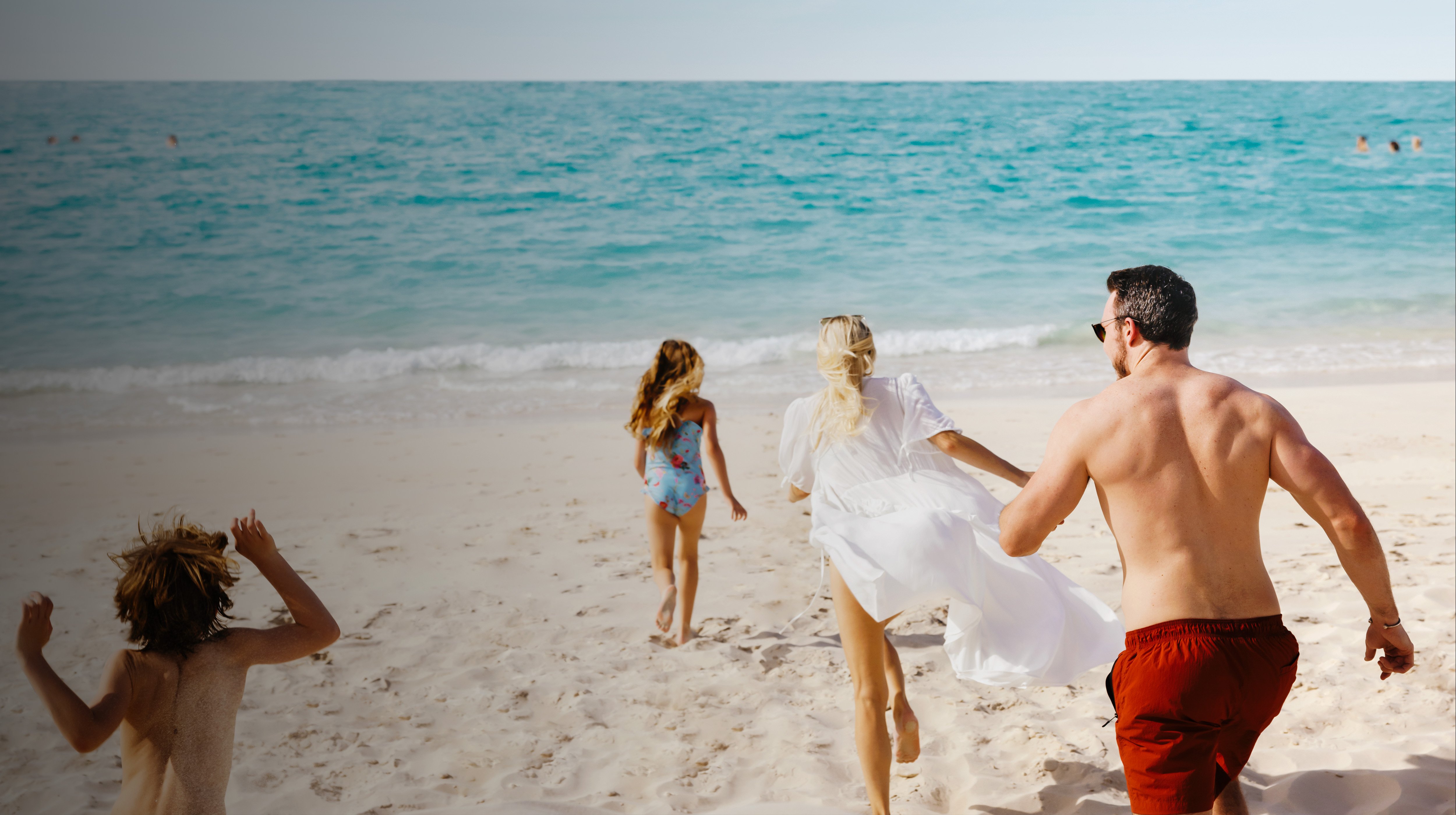 Family running toward the turquoise waters of a pristine beach in Abu Dhabi.