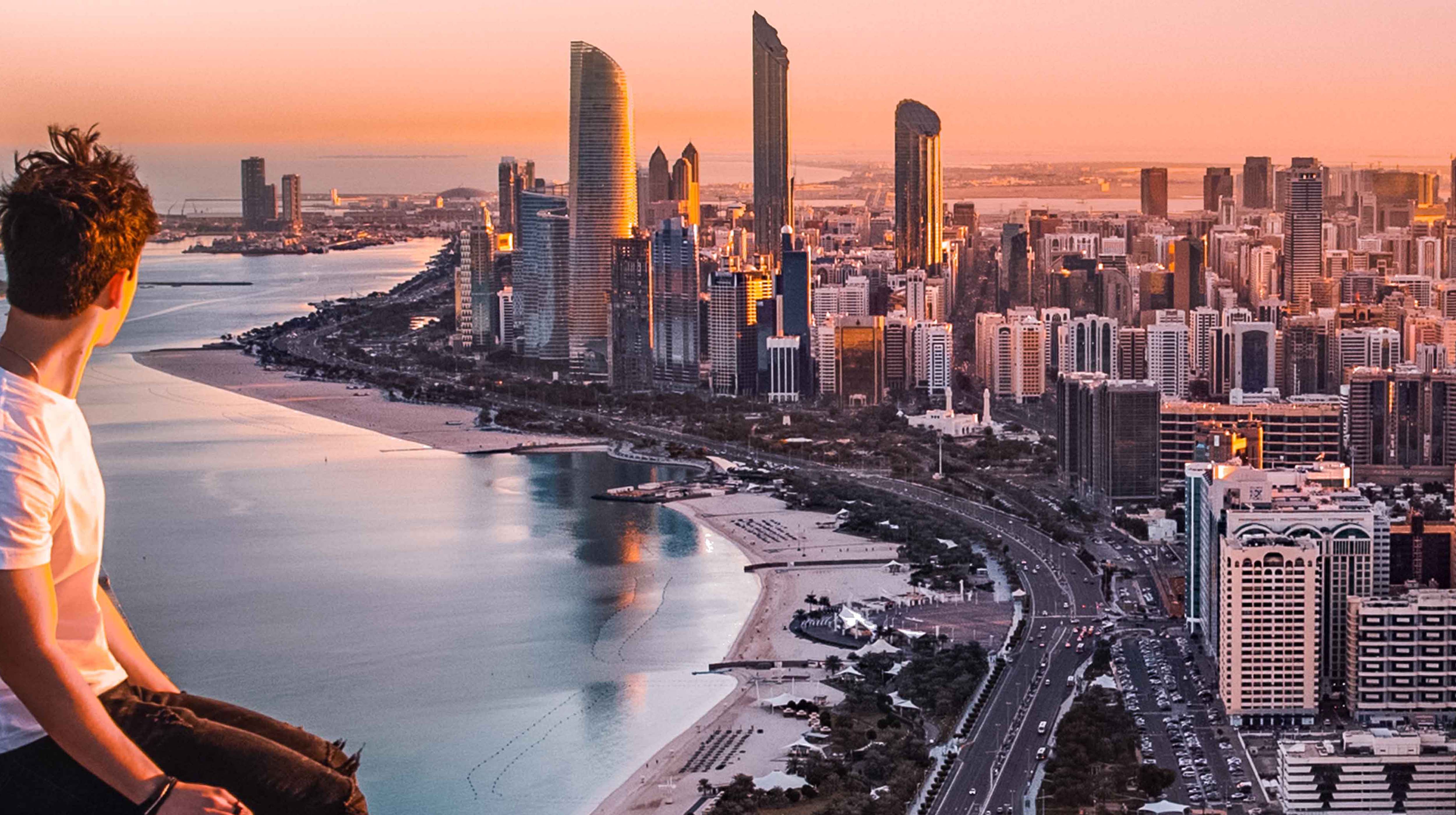 Boy sitting in a high place overlooking the whole of Abu Dhabi's skyline