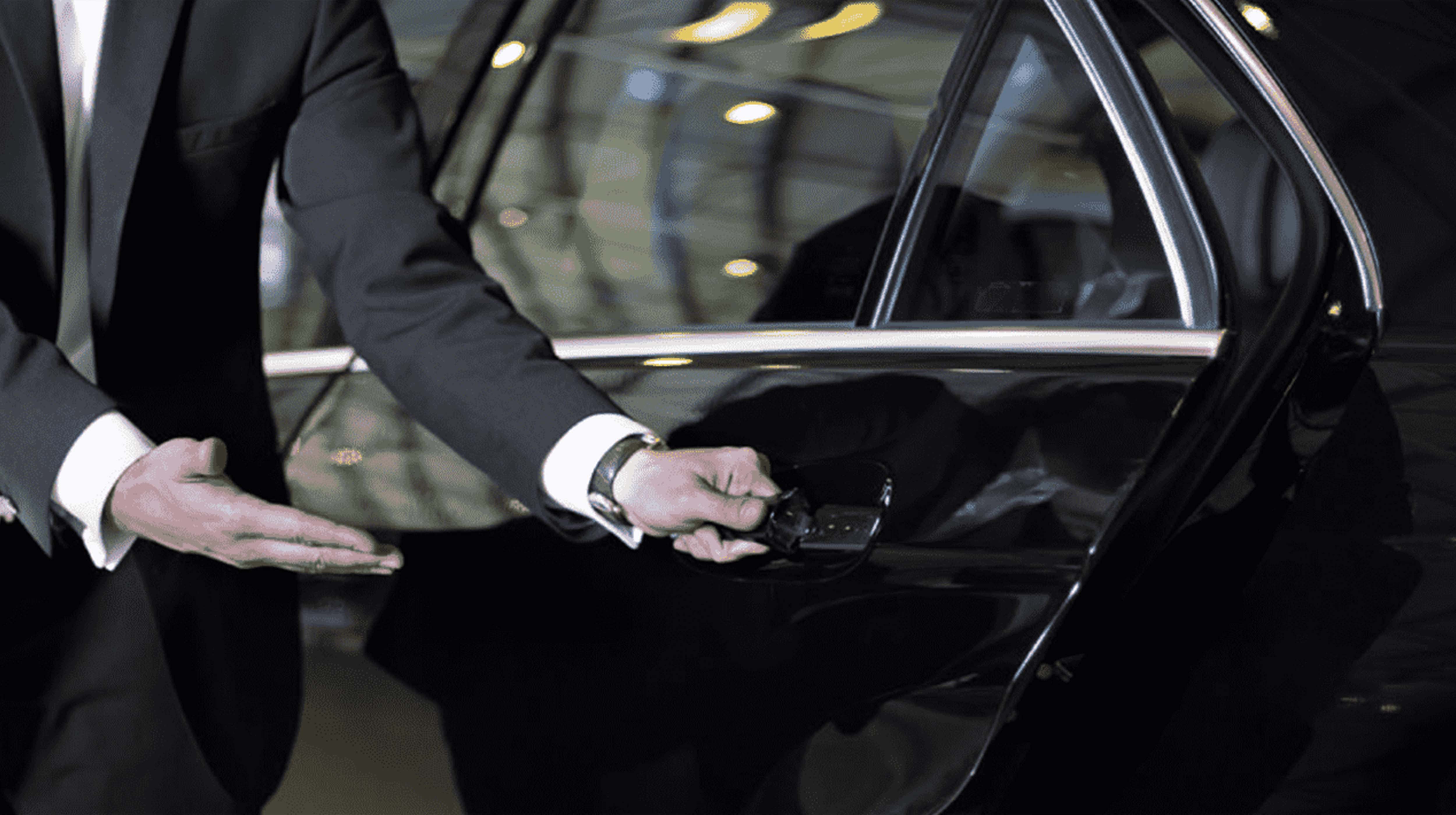 Man wearing a black suit opening the door of a black taxi in Abu Dhabi