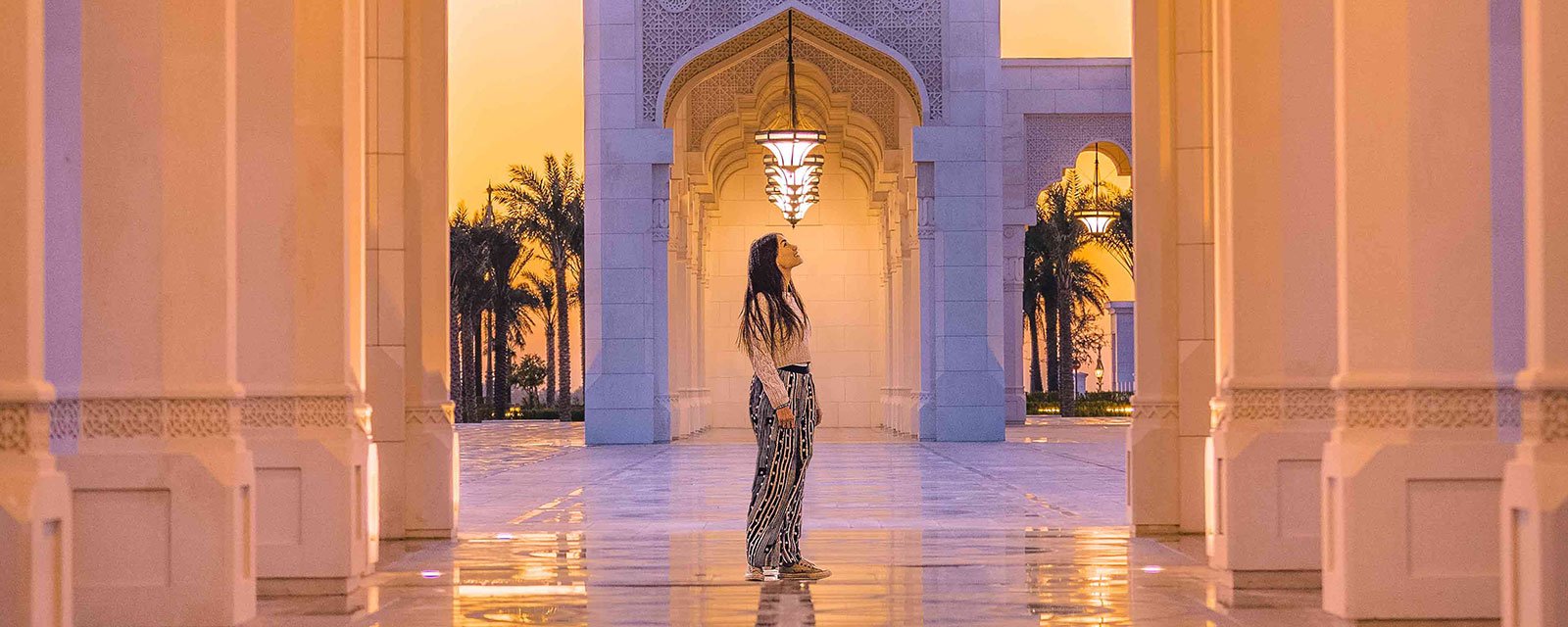 Frau spaziert durch beleuchtete Bogengänge des Qasr Al Watan