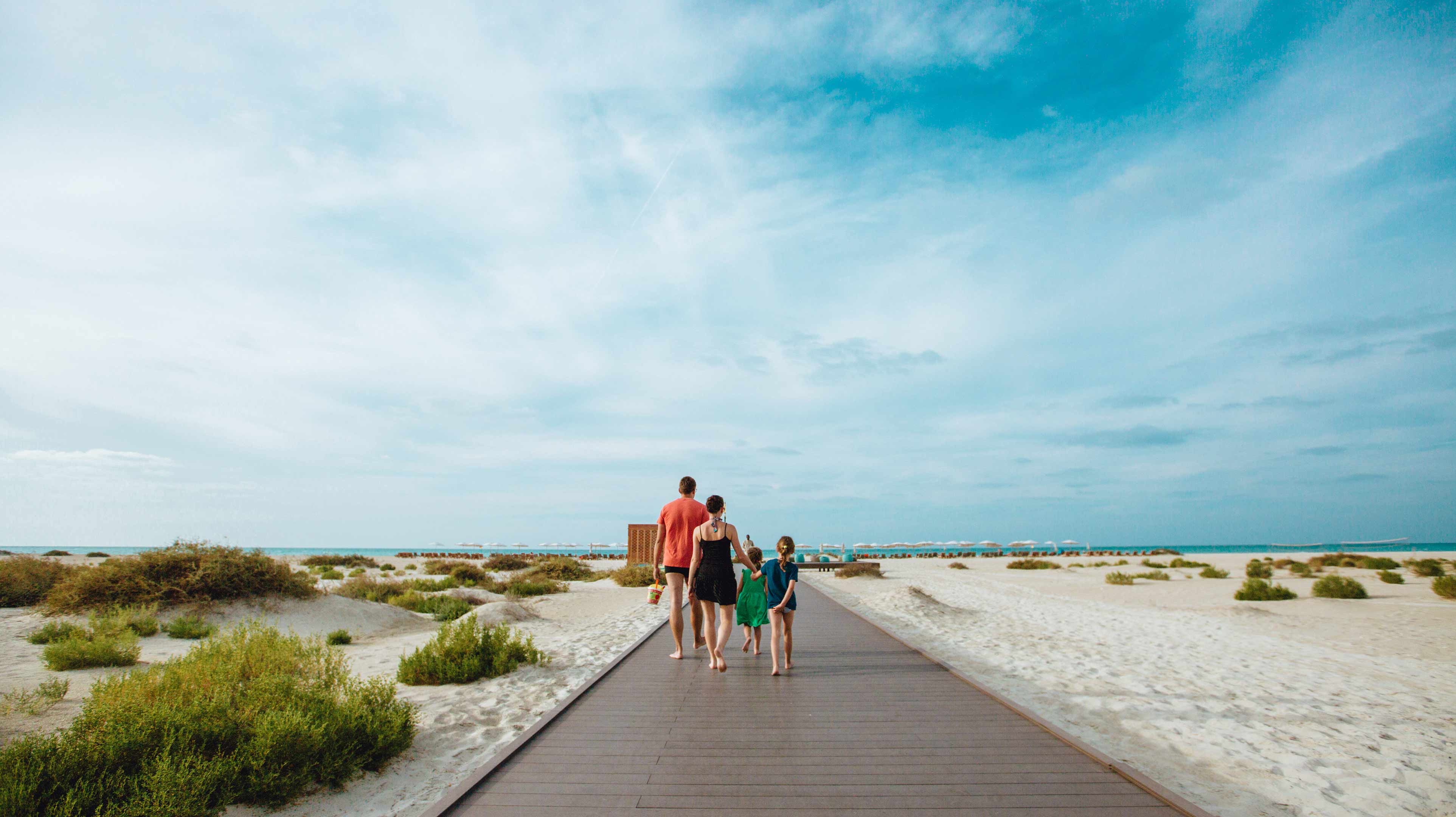  Flânez en famille sur la passerelle de Saadiyat Beach, entre dunes dorées et horizon azur. Un cadre idéal pour une journée de plage paisible et connectée à la nature.