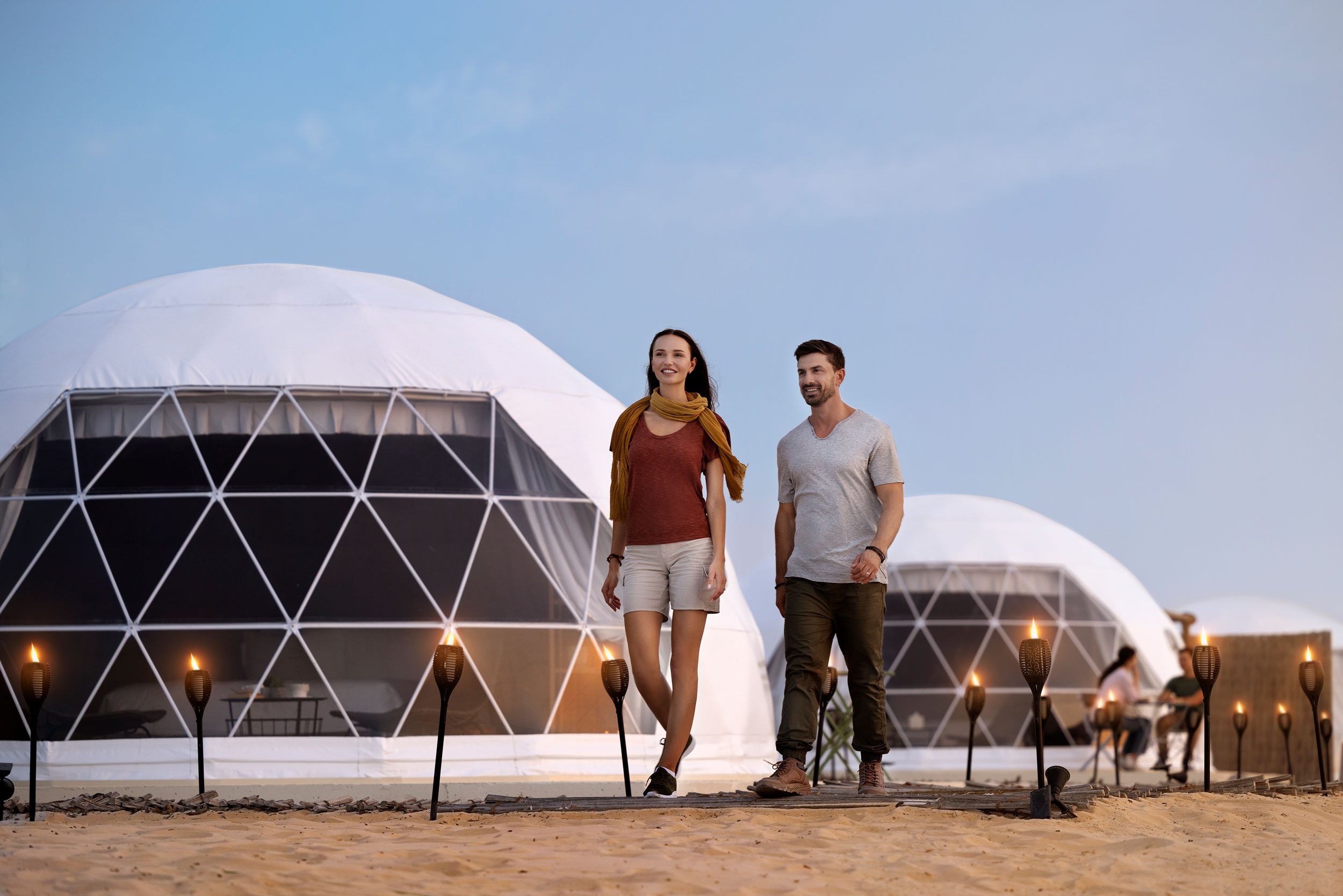 Couple walking outside luxury dome tents at a desert glamping site during sunset in Abu Dhabi.