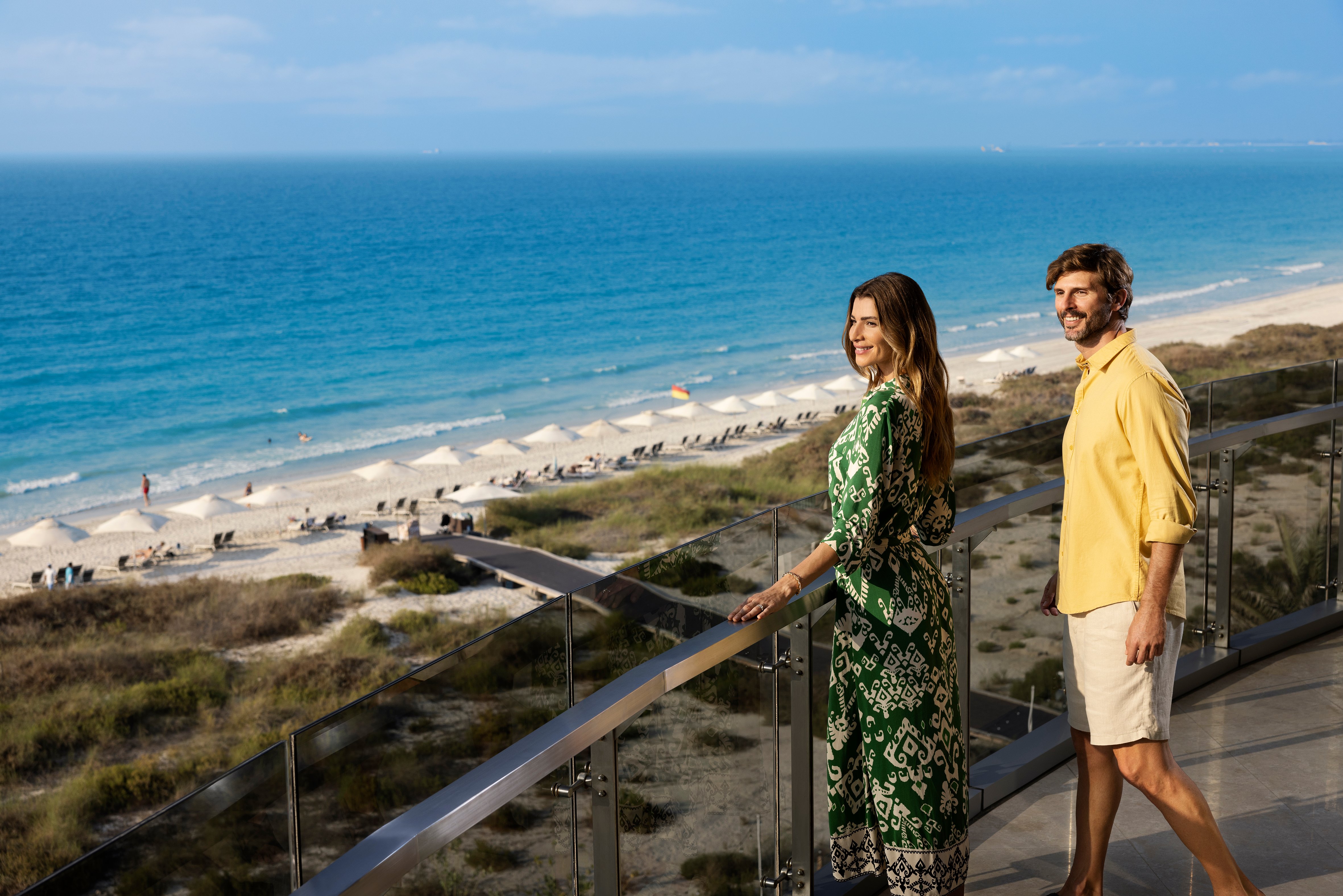 Couple enjoying a serene view of Abu Dhabi’s pristine Jumeirah beach from a luxury resort balcony.