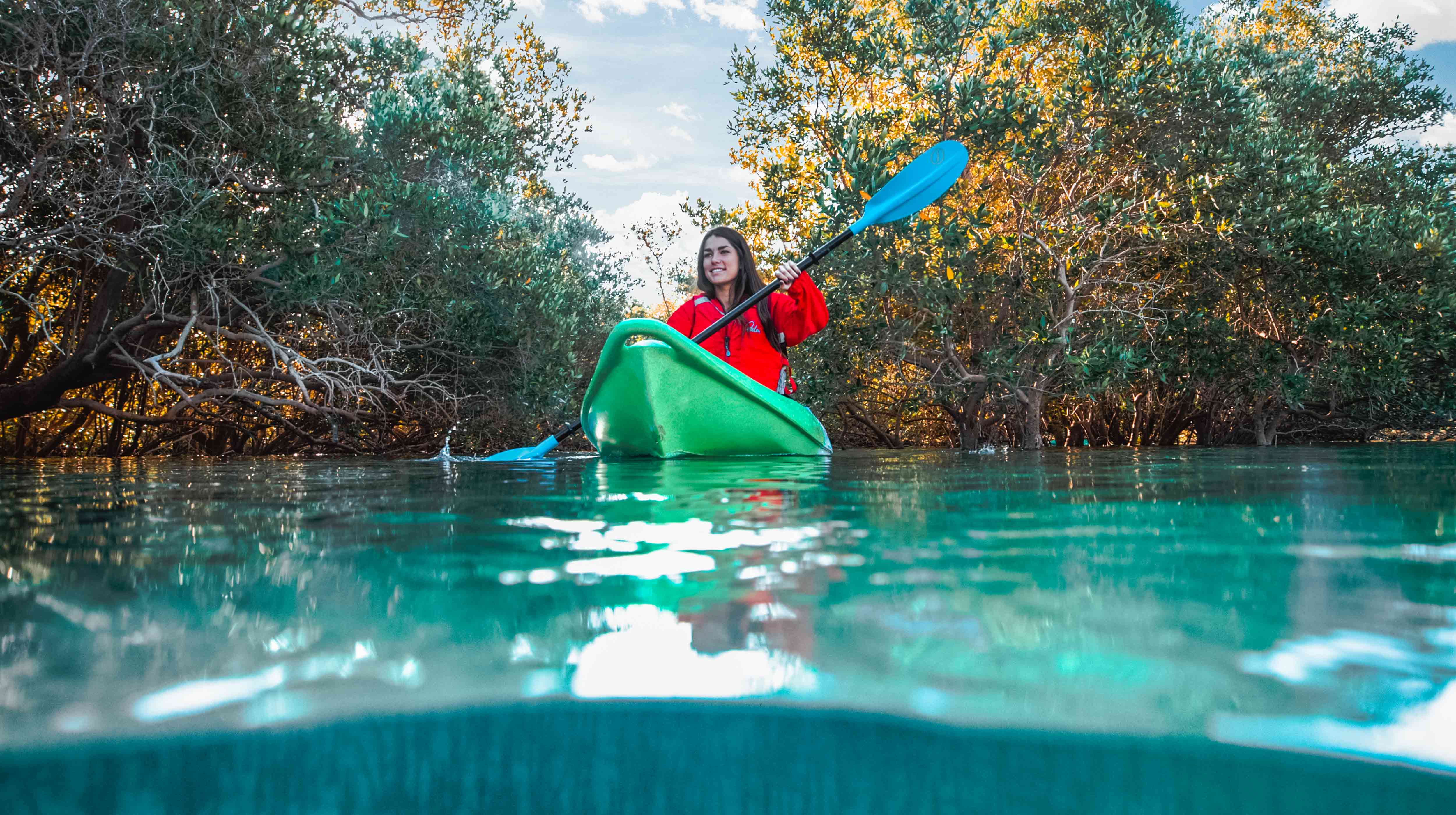 Eine lächelnde junge Frau paddelt in einem grünen Kajak durch die üppig grüne Natur im Mangroven-Nationalpark in Abu Dhabi