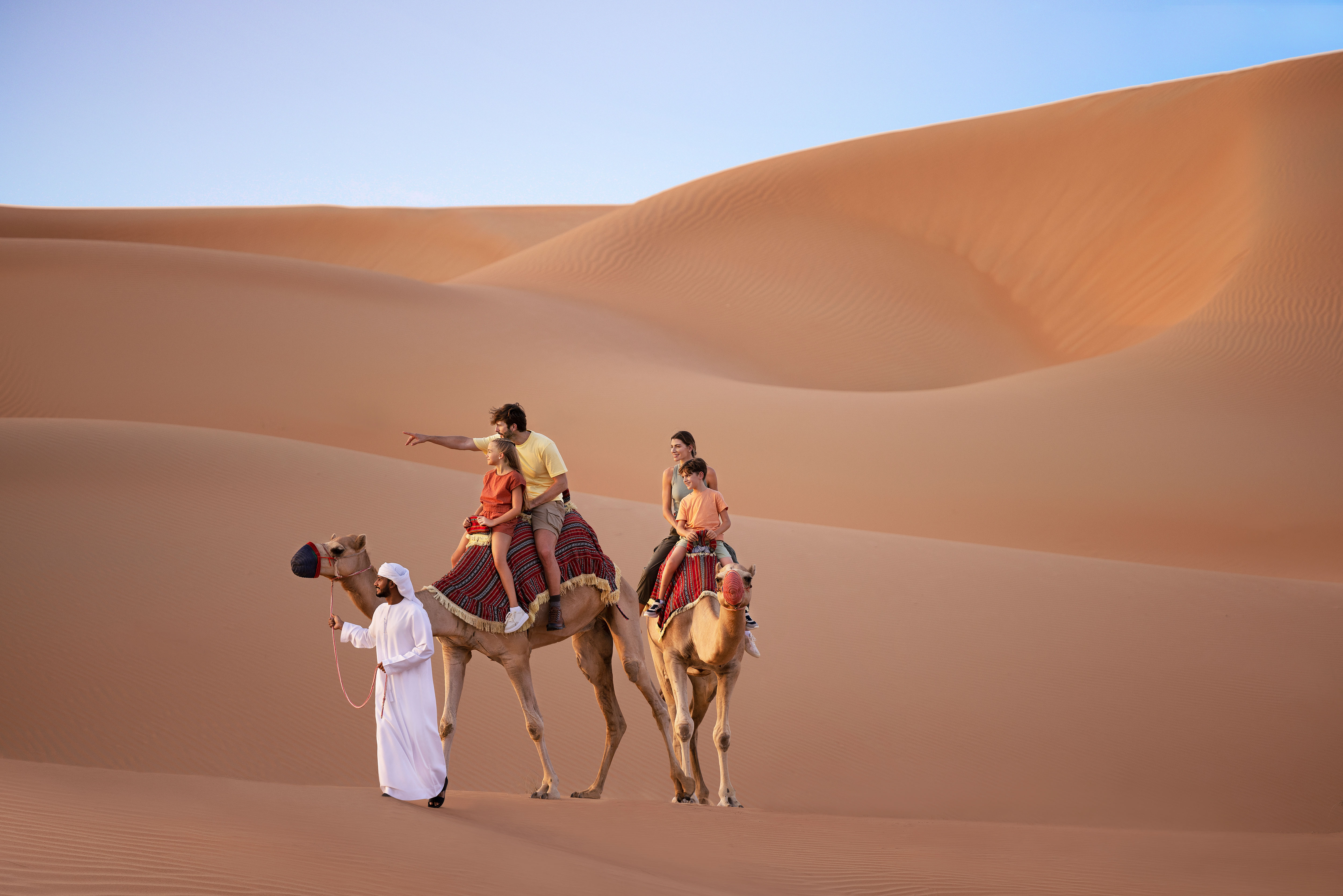 Guide walking a family of 4 on 2 camels in the Abu Dhabi sand dunes