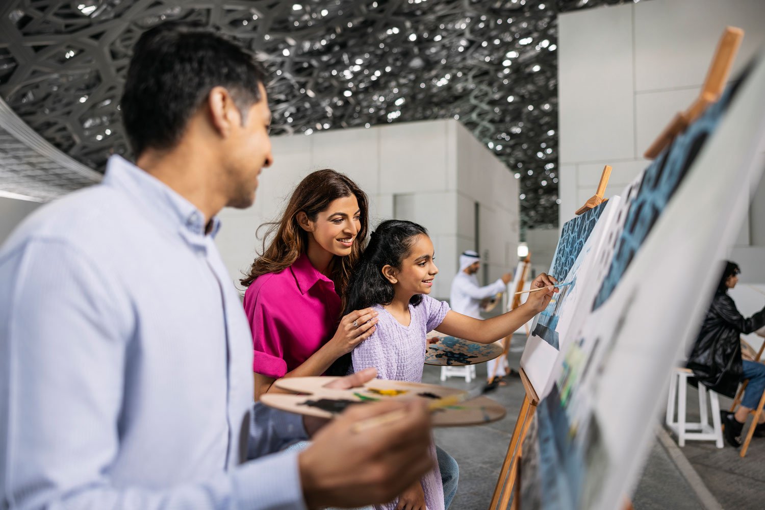  Dans un cadre artistique, une famille partage un moment créatif, peignant ensemble au Louvre Abu Dhabi, reflet de la culture et des émotions.