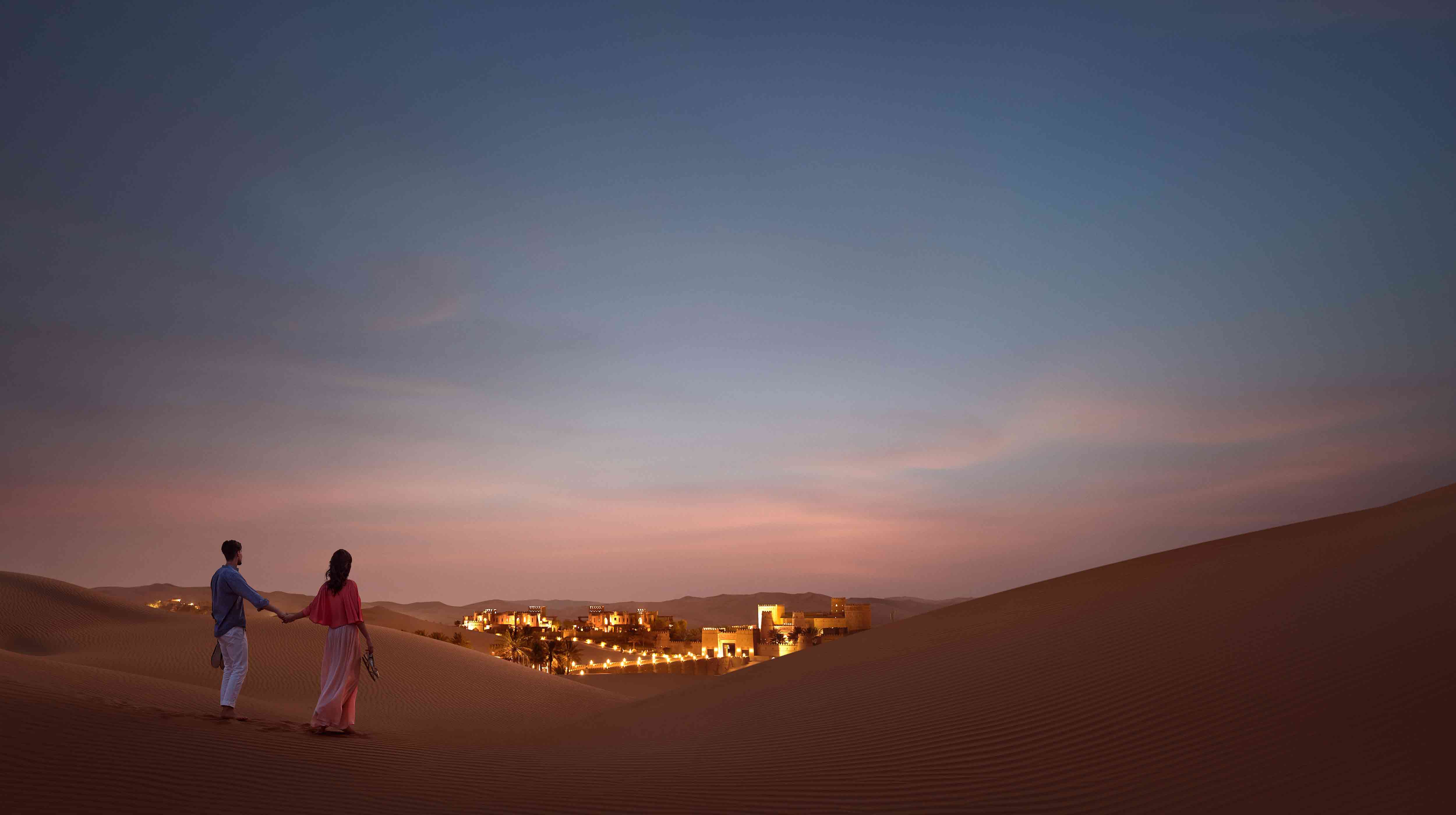  Un couple se tient la main dans le désert, admirant la beauté d'Abu Dhabi au crépuscule.