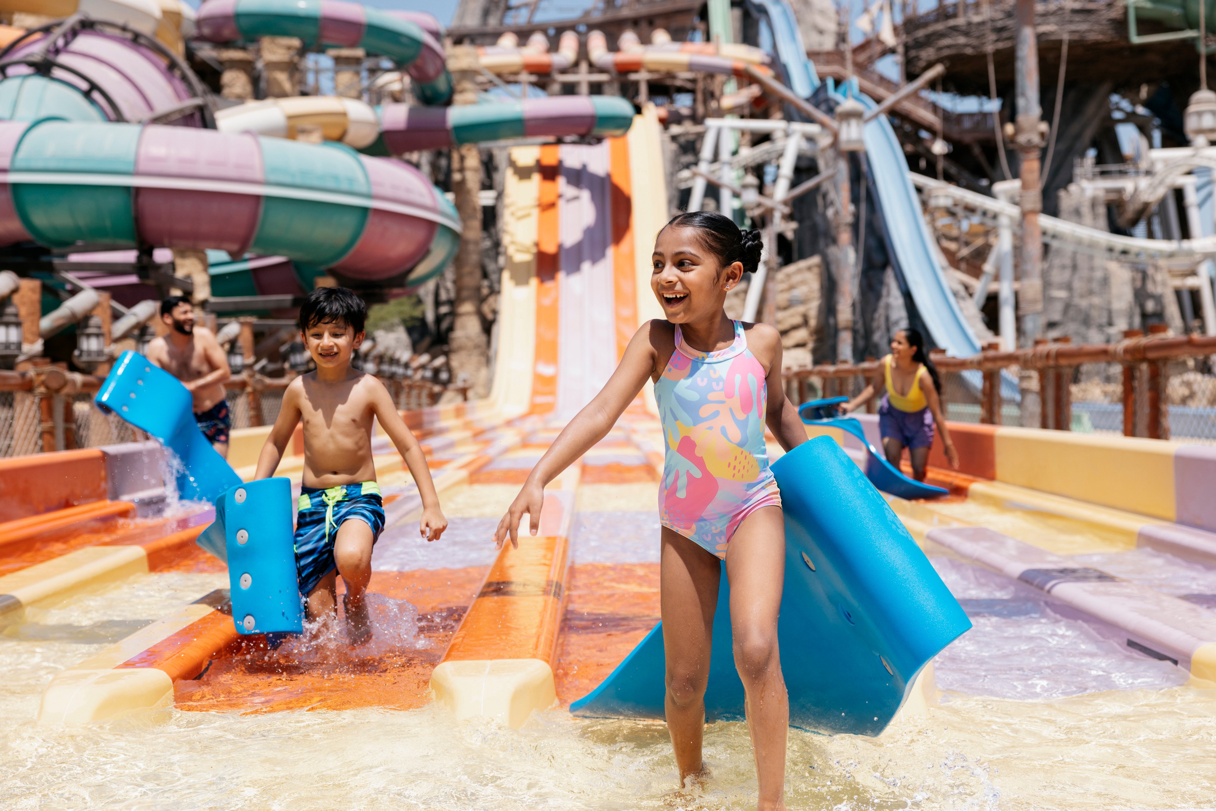 Aufgeregte Familie mit lächelnden kleinen Kindern, die eine Wasserrutsche in Yas Island Abu Dhabi genießen