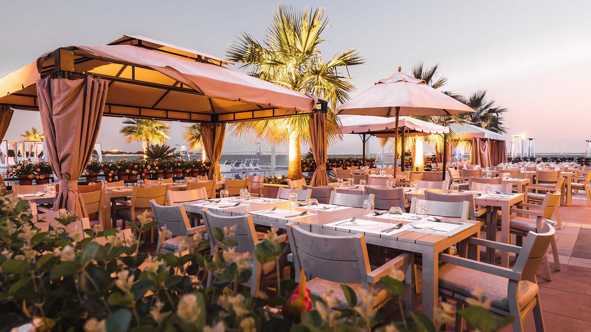 Tables in Abu Dhabi restaurant at dusk with lights reflecting off trees